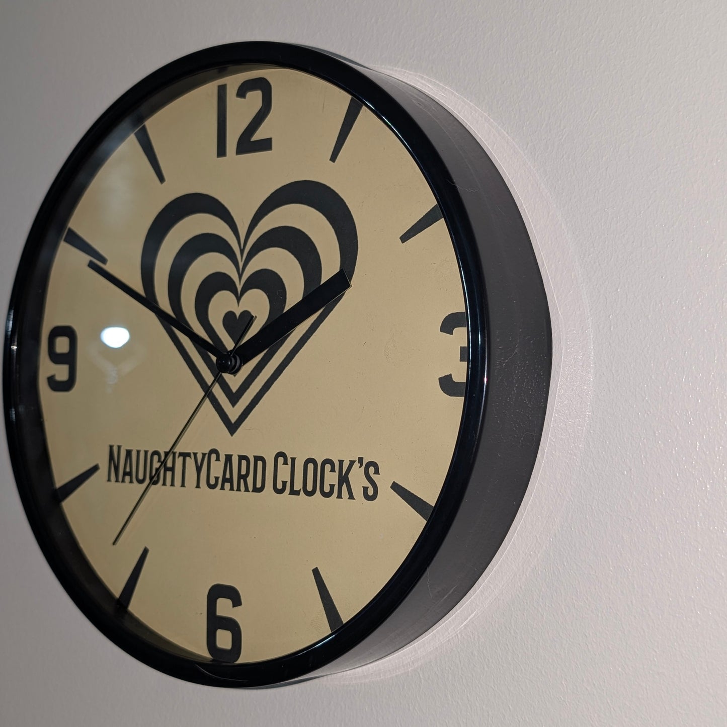 Right side view of black plastic wall clock, on plain wall