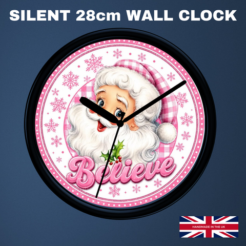 A round wall clock with a black frame and a festive Santa design. The clock face is white with pink gingham accents, snowflakes, and the word 'Believe' in pink script.