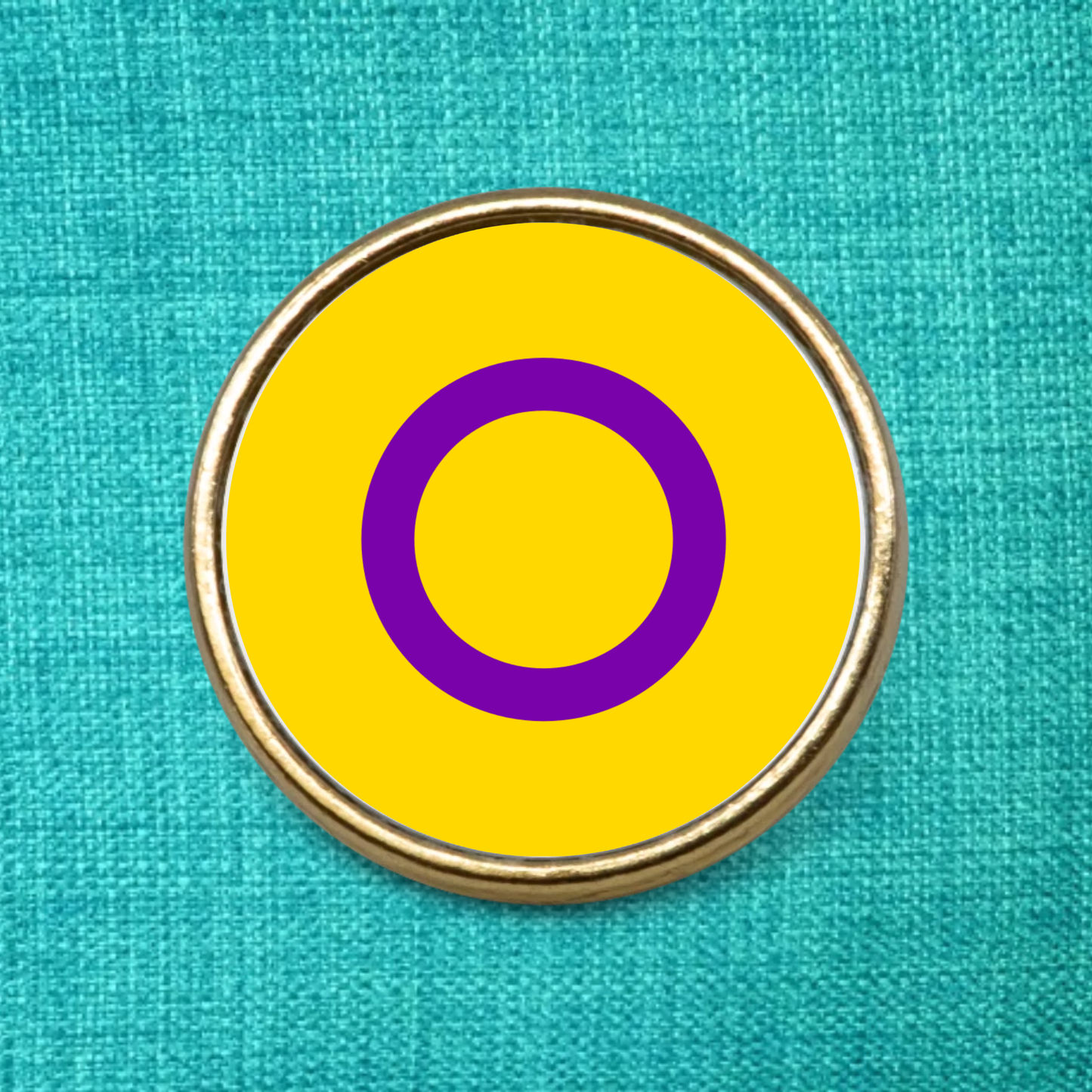 Round intersex badge yellow with purple circle on a teal fabric background