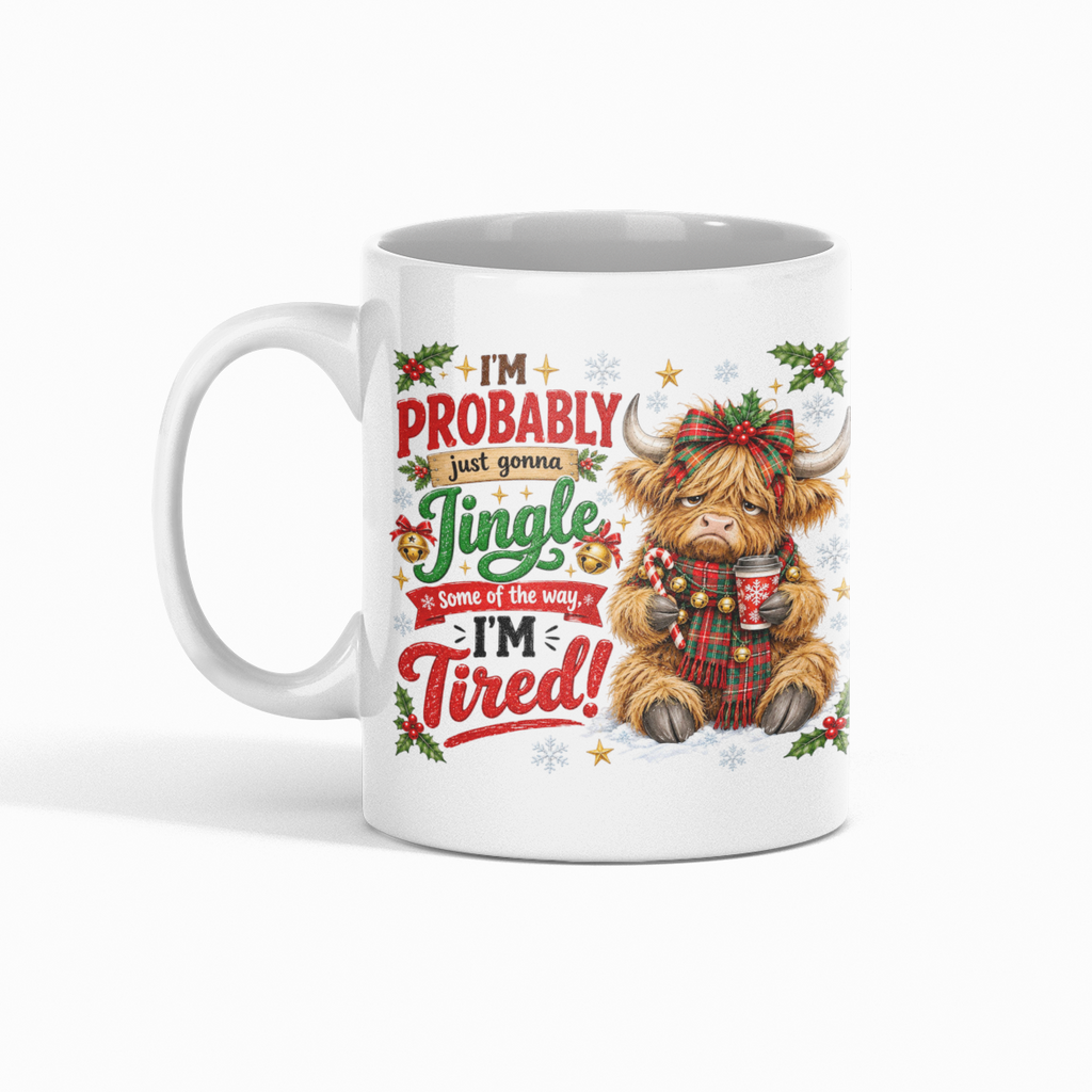 A white ceramic mug featuring a festive Christmas graphic of a Scottish highland cow holding a mug and surrounded by holiday text that reads 'I'm Probably Jingle Dandy Because I'm Tired!'.