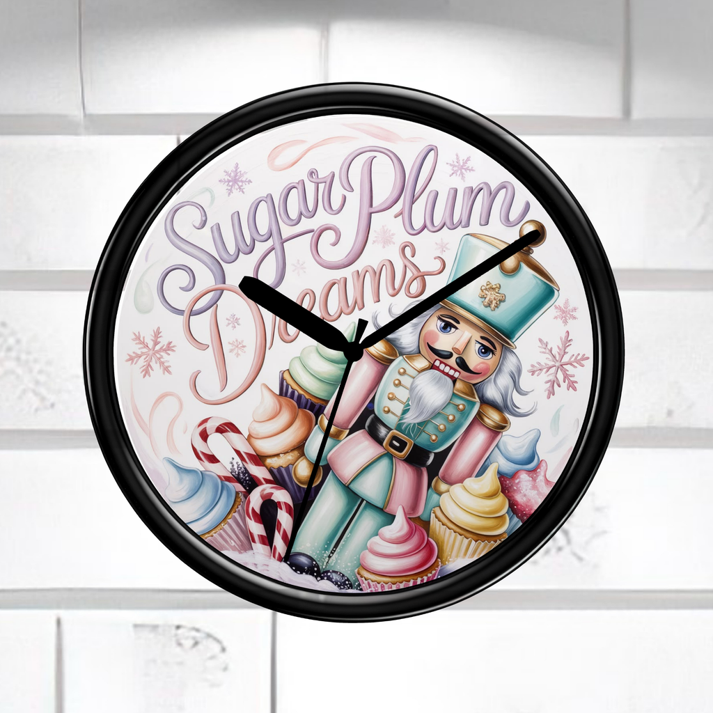 A round wall clock with a black frame and a whimsical nutcracker illustration on the face. The clock face features the text 'Sugar Plum Dreams' in purple script, along with cupcakes, candy canes, snowflakes, and pastel-colored details.