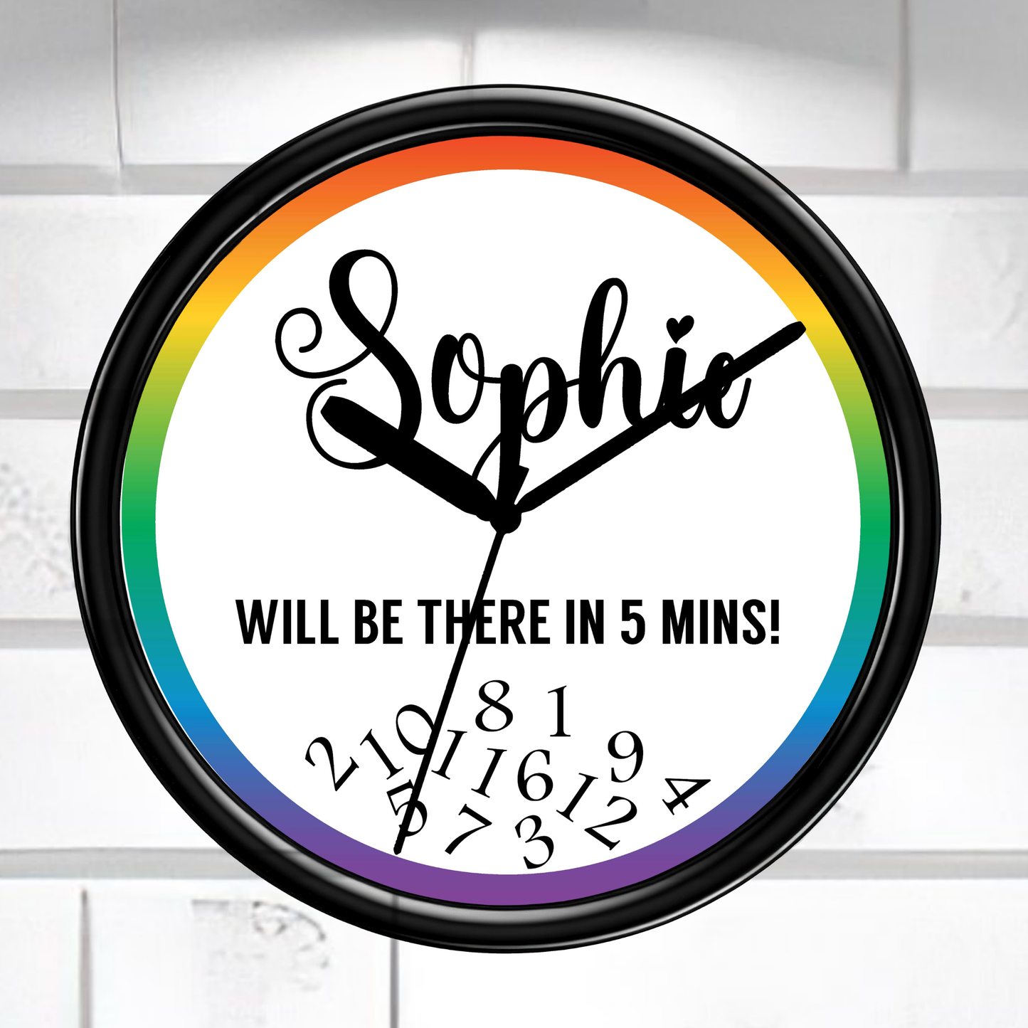 Wall clock with rainbow border and text 'Sophie WILL BE THERE IN 5 MINS!' on a white brick wall background