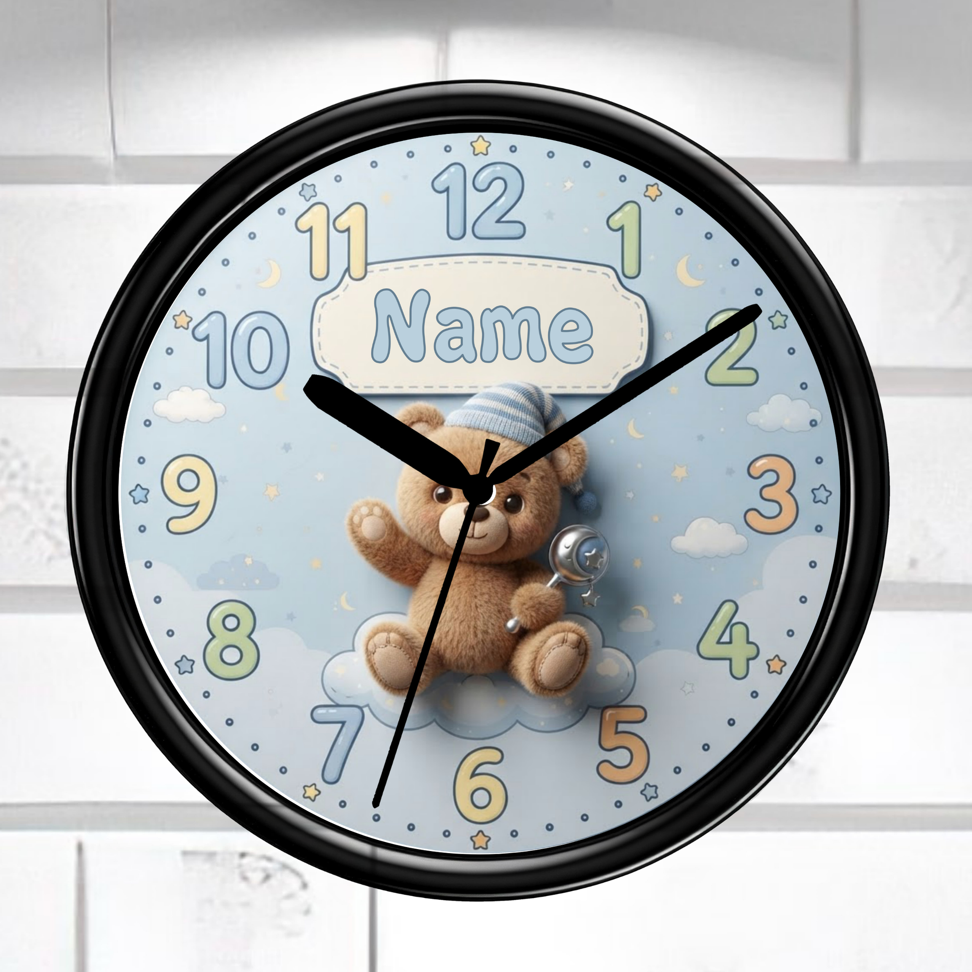 A round wall clock with a black frame and a light blue face featuring a teddy bear, clouds, stars, and colorful numbers. The center includes a customizable name patch that reads 'Name'.