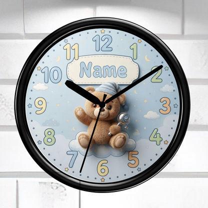 A round wall clock with a black frame and a light blue face featuring a teddy bear, clouds, stars, and colorful numbers. The center includes a customizable name patch that reads 'Name'.