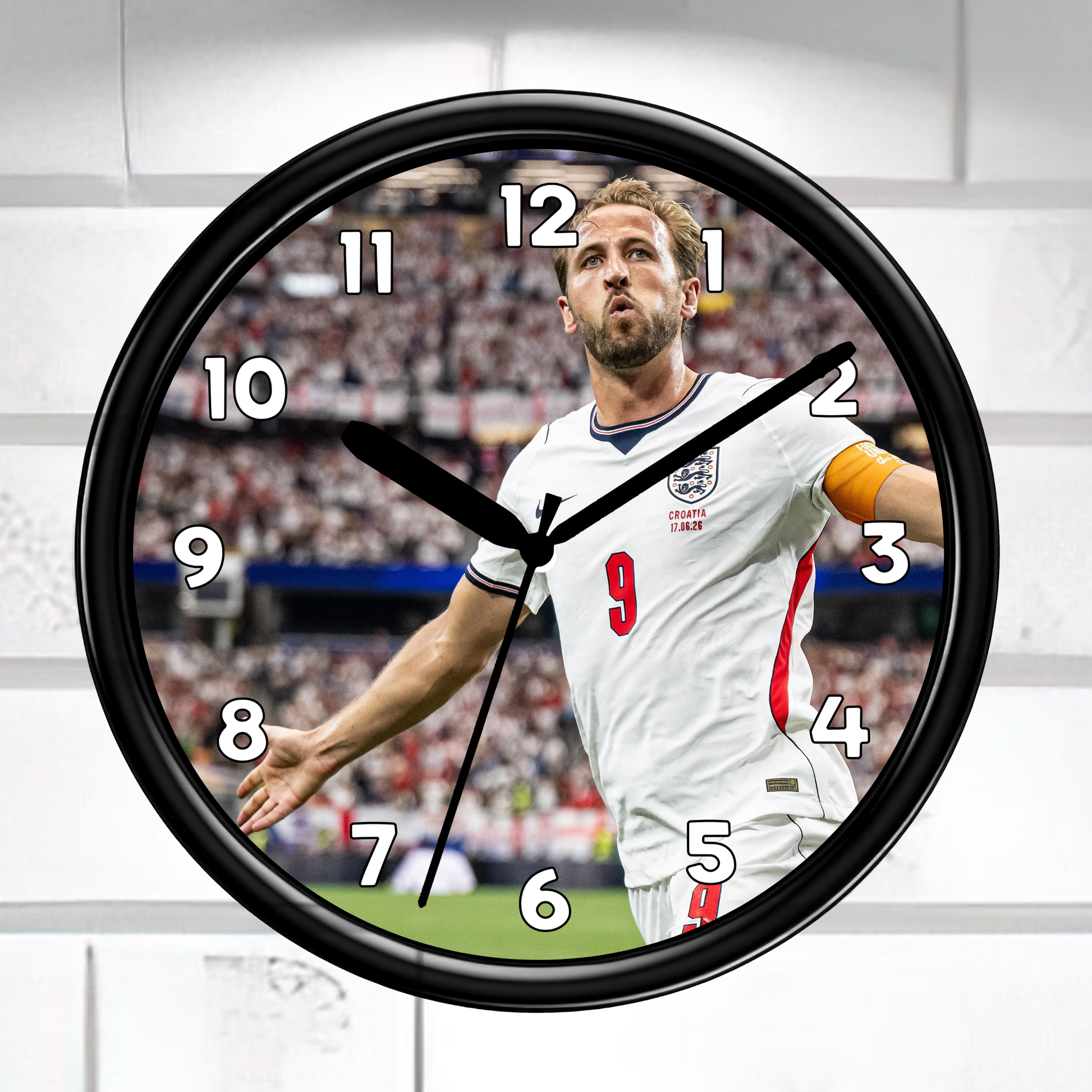 A round wall clock with a black frame and a printed soccer player design on the face, shown against a light gray paneled background.
