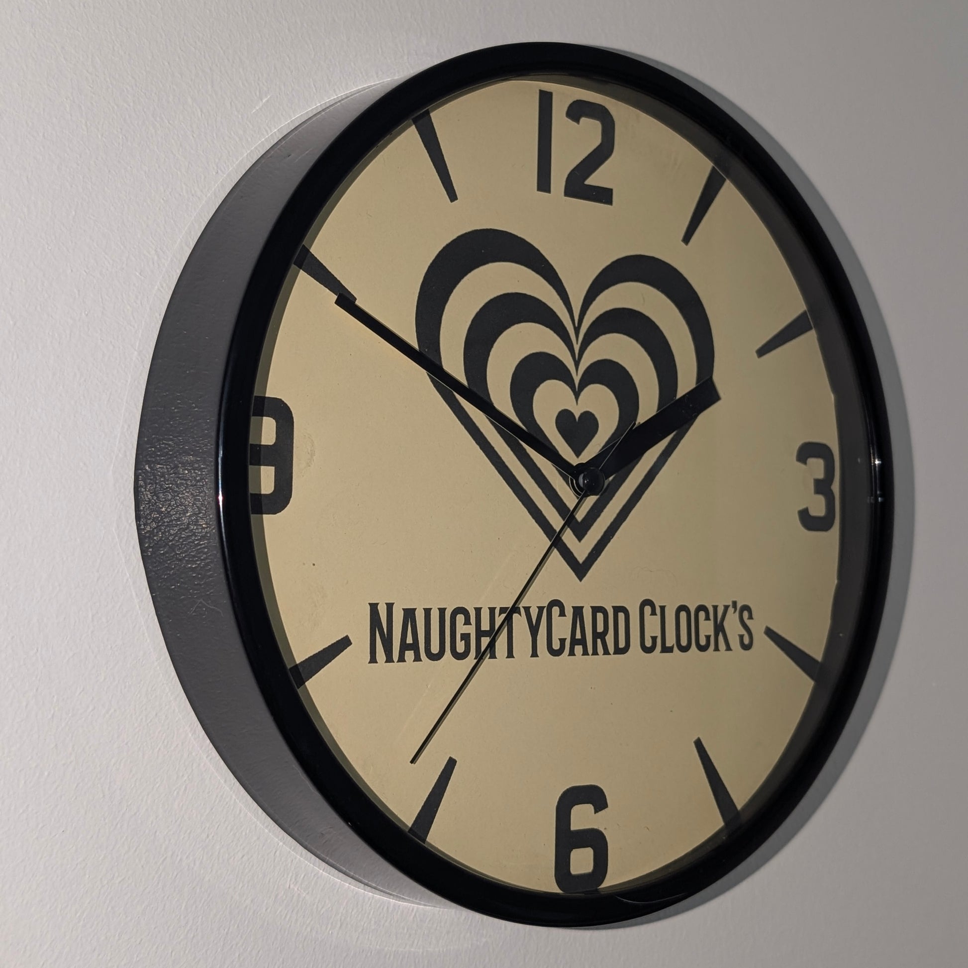 Left side view of black plastic wall clock from Naughty Card on a plain white background
