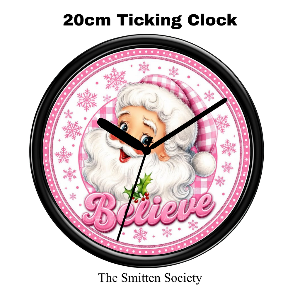 A round Christmas wall clock with a black frame, featuring an illustration of Santa Claus, pink snowflakes, the word 'Believe' in pink script, and text above and below reading '20cm Ticking Clock' and 'The Smitten Society'.