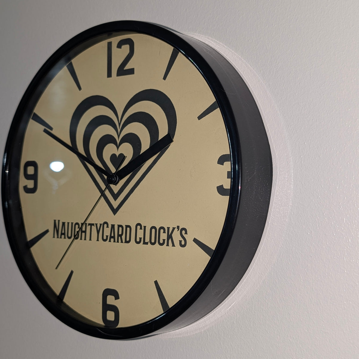 Right side view of black plastic wall clock, on plain wall