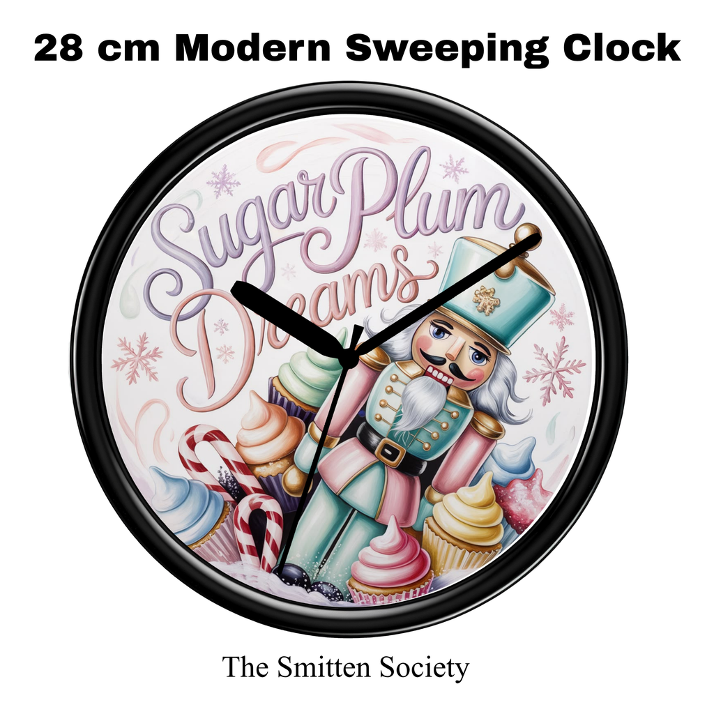 A 28 cm modern wall clock with a black frame and a whimsical holiday illustration featuring a nutcracker, cupcakes, candy canes, and the text 'Sugar Plum Dreams'. The clock is shown on a plain white background with text overlays reading '28 cm Modern Sweeping Clock' at the top and 'The Smitten Society' at the bottom.