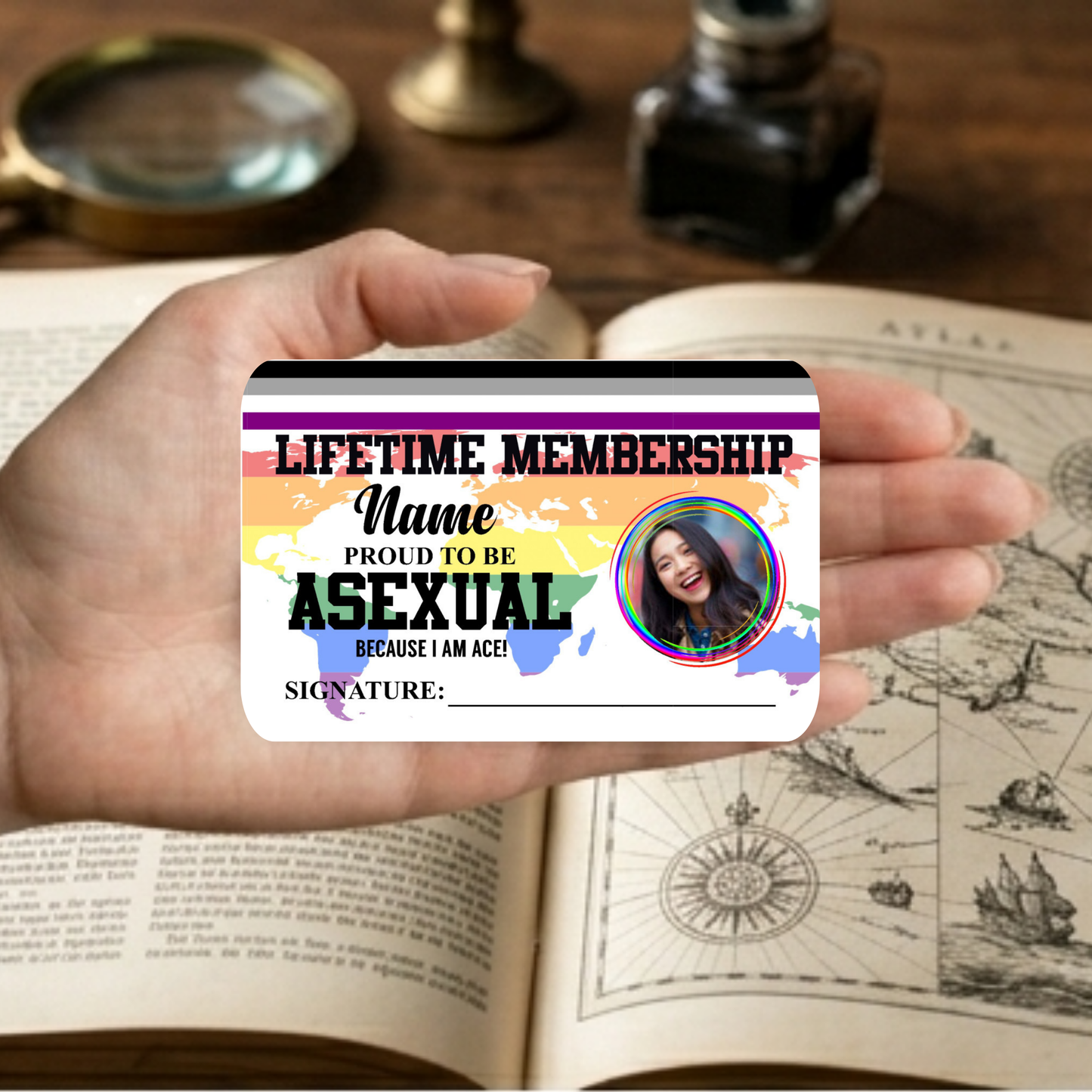 Hand holding a 'Lifetime Membership: Proud to be Asexual' card on an open book with vintage items.