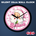 A round wall clock with a black frame and a festive Santa design. The clock face is white with pink gingham accents, snowflakes, and the word 'Believe' in pink script.