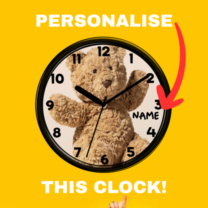 A round wall clock with a teddy bear printed on the face and black numerals, shown on a bright yellow background with the words 'PERSONALISE THIS CLOCK!' and a red arrow pointing to the clock.