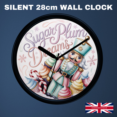 A round wall clock with a black frame and a whimsical nutcracker illustration on a white background, featuring the words 'Sugar Plum Dreams' and decorated with cupcakes, candy canes, and snowflakes. The clock is shown against a dark blue background with the text 'SILENT 28cm WALL CLOCK' at the top and a small 'Made in UK' flag graphic in the bottom right corner.