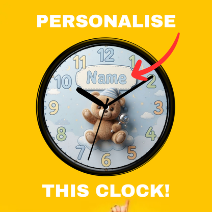 A round personalized children's wall clock with a black frame, light blue face, teddy bear illustration, and colorful numbers. Large white text reads 'PERSONALISE' at the top and 'THIS CLOCK!' at the bottom, with a red arrow pointing to the name customization area.