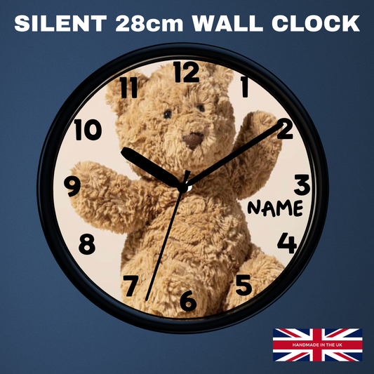 A round wall clock with a black frame and a teddy bear face printed on the dial, shown against a dark blue background. Large white text at the top reads 'SILENT 28cm WALL CLOCK', and a small 'Made in UK' flag graphic appears in the bottom right corner.