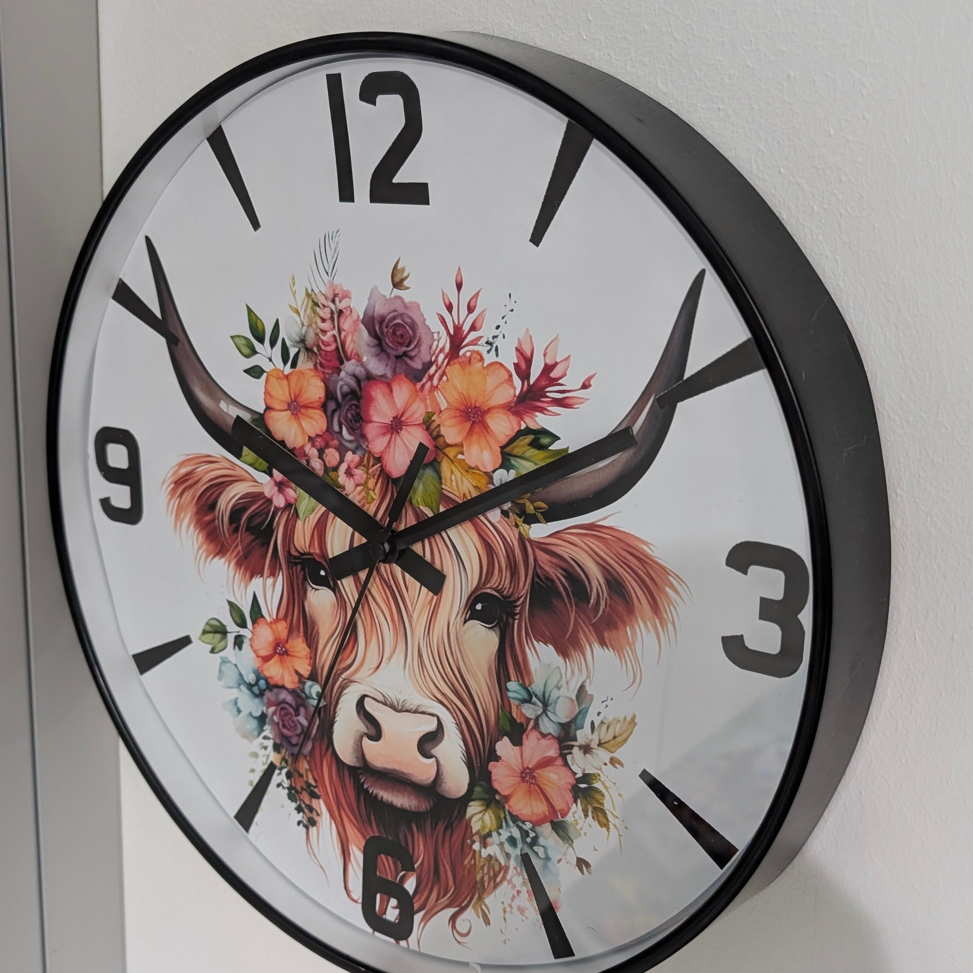Wall clock with a decorative design of a cow's face surrounded by flowers on a white background.