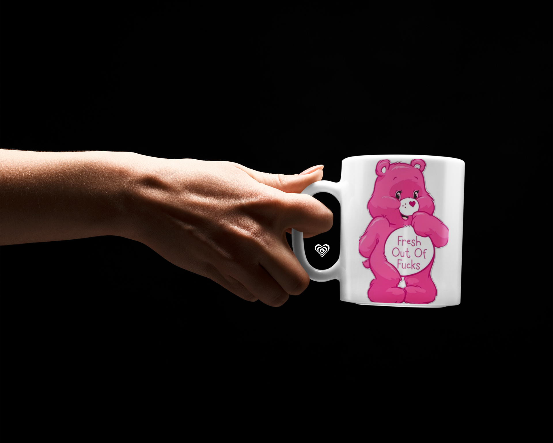 Hand holding a mug with a pink bear design and 'fresh out of fu*ks' text on a black background