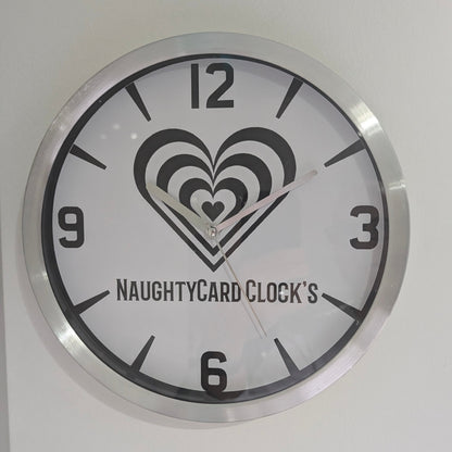 A silver metallic wall clock featuring an image of NaughtyCard logo and numbers, predominantly in black and white with a silver or metallic accent. Metallic Wall Clock from NaughtyCard