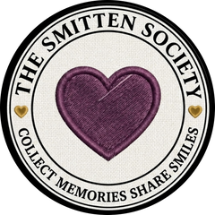 A circular embroidered patch design featuring a central purple heart on a cream fabric-textured background, surrounded by a black and white border with the text 'THE SMITTEN SOCIETY' and 'COLLECT MEMORIES SHARE SMILES', plus two small gold hearts.