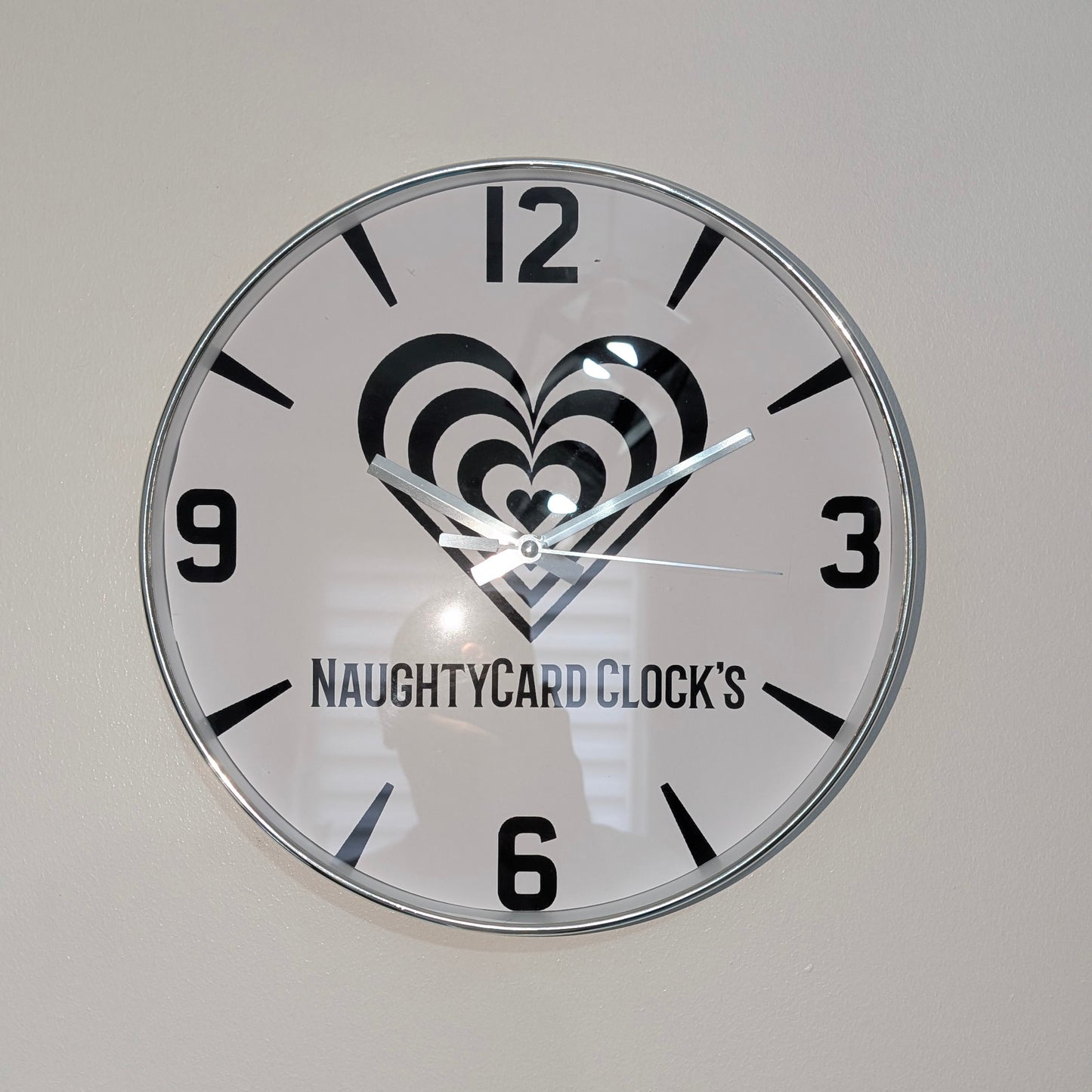 Silver Wall clock with heart design and 'NaughtyCard Clock's' branding on a plain background
