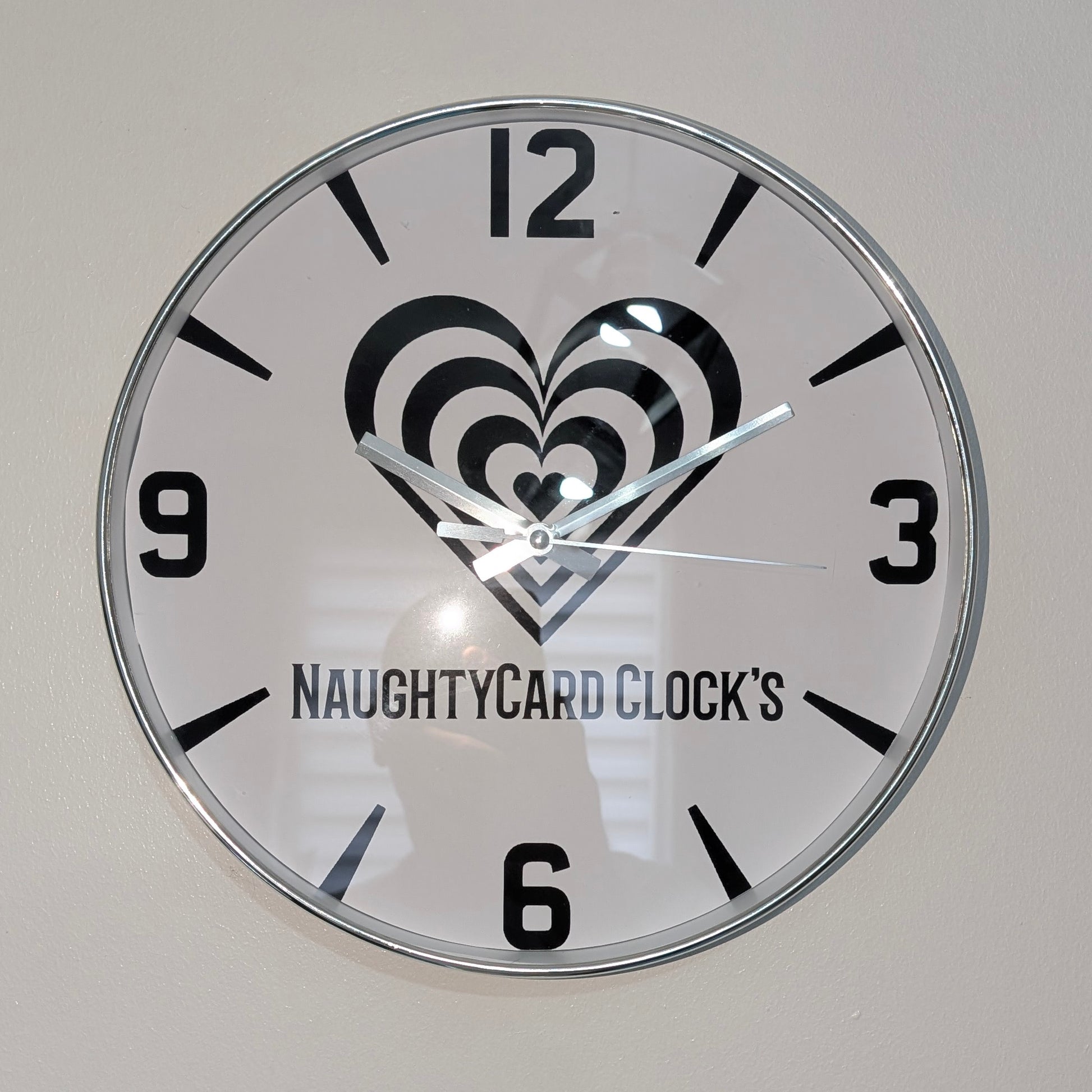 Wall clock with heart design and 'NAUGHTYCARD CLOCK'S' branding on a plain background
